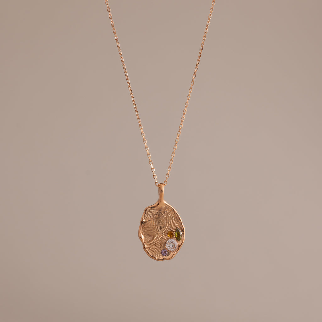 The Organic Fingerprint Multi Birthstone Necklace in Rose Gold features a unique textured charm with multiple sparkling stones on a delicate chain—an elegant, personalized jewelry piece perfect for any occasion.