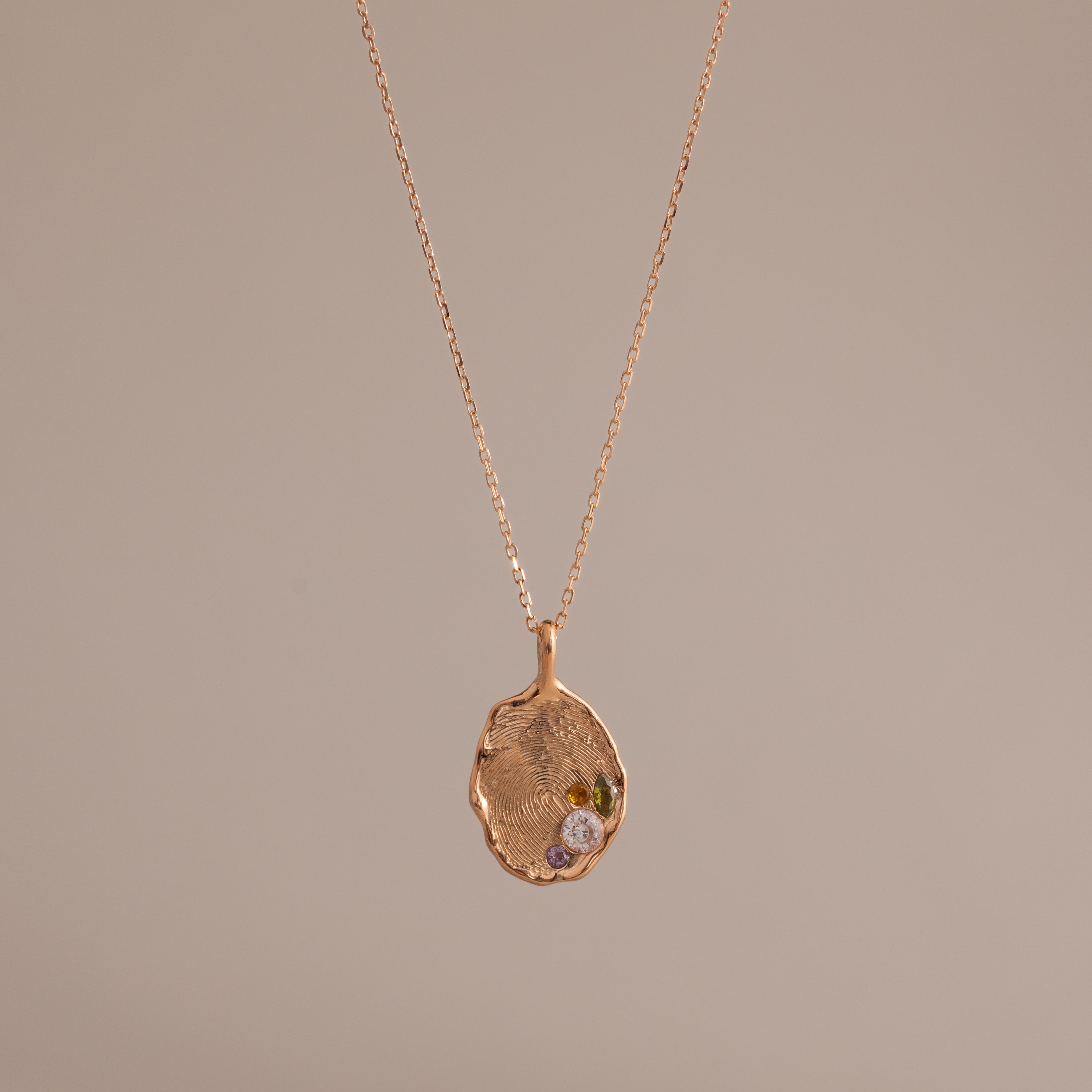 The Organic Fingerprint Multi Birthstone Necklace in Rose Gold features a unique textured charm with multiple sparkling stones on a delicate chain—an elegant, personalized jewelry piece perfect for any occasion.
