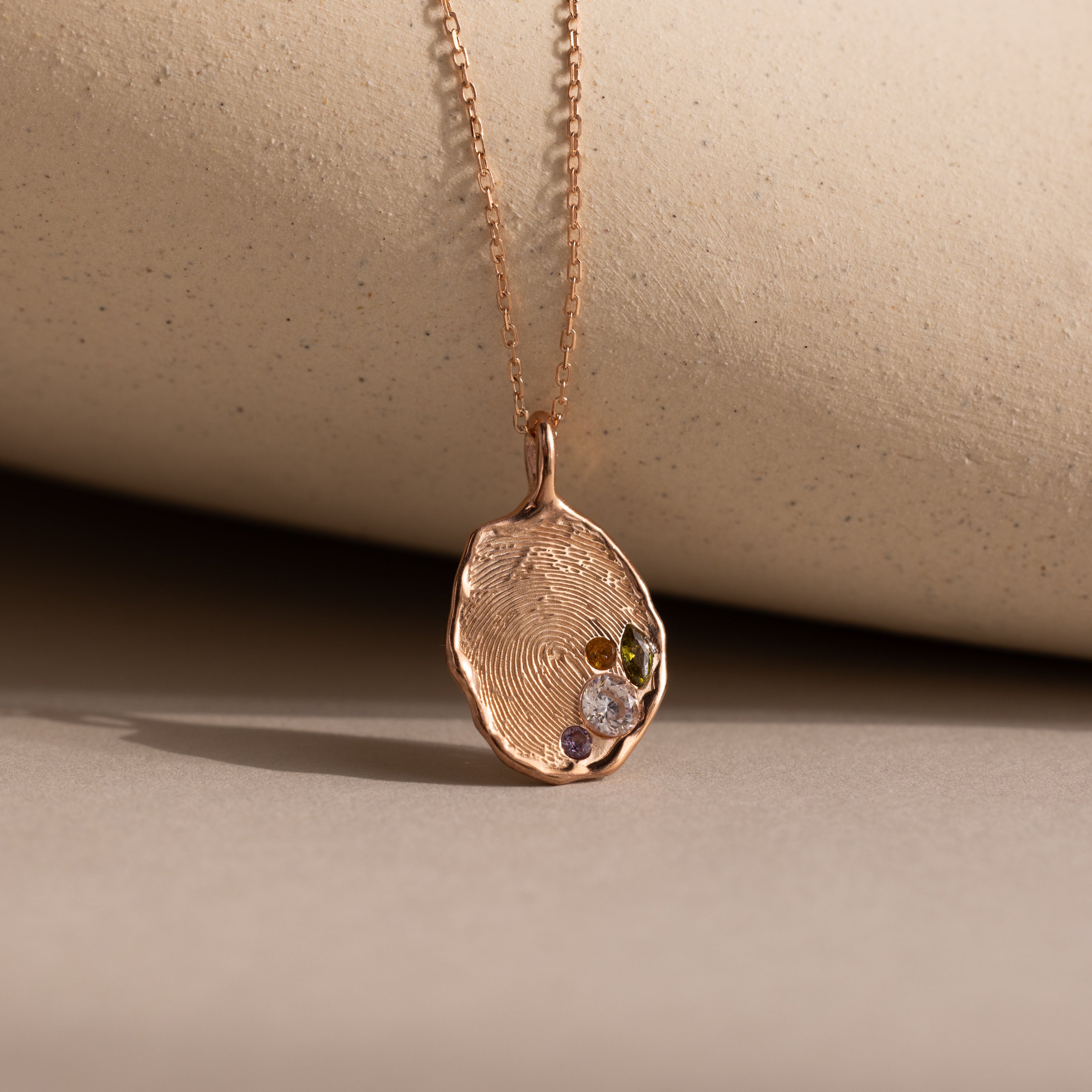 The Organic Fingerprint Multi Birthstone Necklace in Rose Gold is displayed against a beige background—a stunning personalized necklace perfect as a birthstone keepsake.