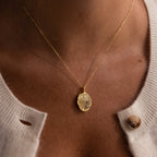 A close-up of the Organic Fingerprint Multi Birthstone Necklace in 18K Gold, featuring small gems, worn over a cream-colored sweater.