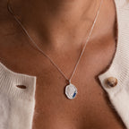 The Organic Fingerprint Multi Birthstone Necklace, featuring blue stones, is a stunning silver pendant keepsake—shown here layered over a white knit sweater for a personalized touch.