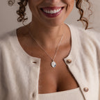 Smiling woman wearing a cream cardigan and the Organic Fingerprint Multi Birthstone Necklace in Sterling Silver, pendant visible, shown from shoulders to mouth.