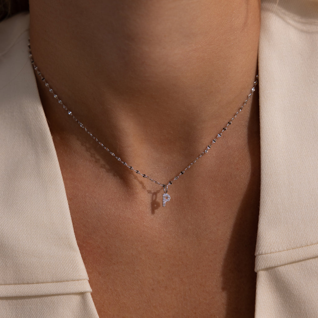 A Dainty Pave Letter Necklace in Sterling Silver rests on a woman's neck, shown close up against a cream blazer.