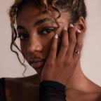 Woman with curly hair touches her face, wearing a black top and highlighting the Black Baguette Diamond Ring in Sterling Silver, featuring a striking baguette-cut centerpiece for a vintage-inspired look.