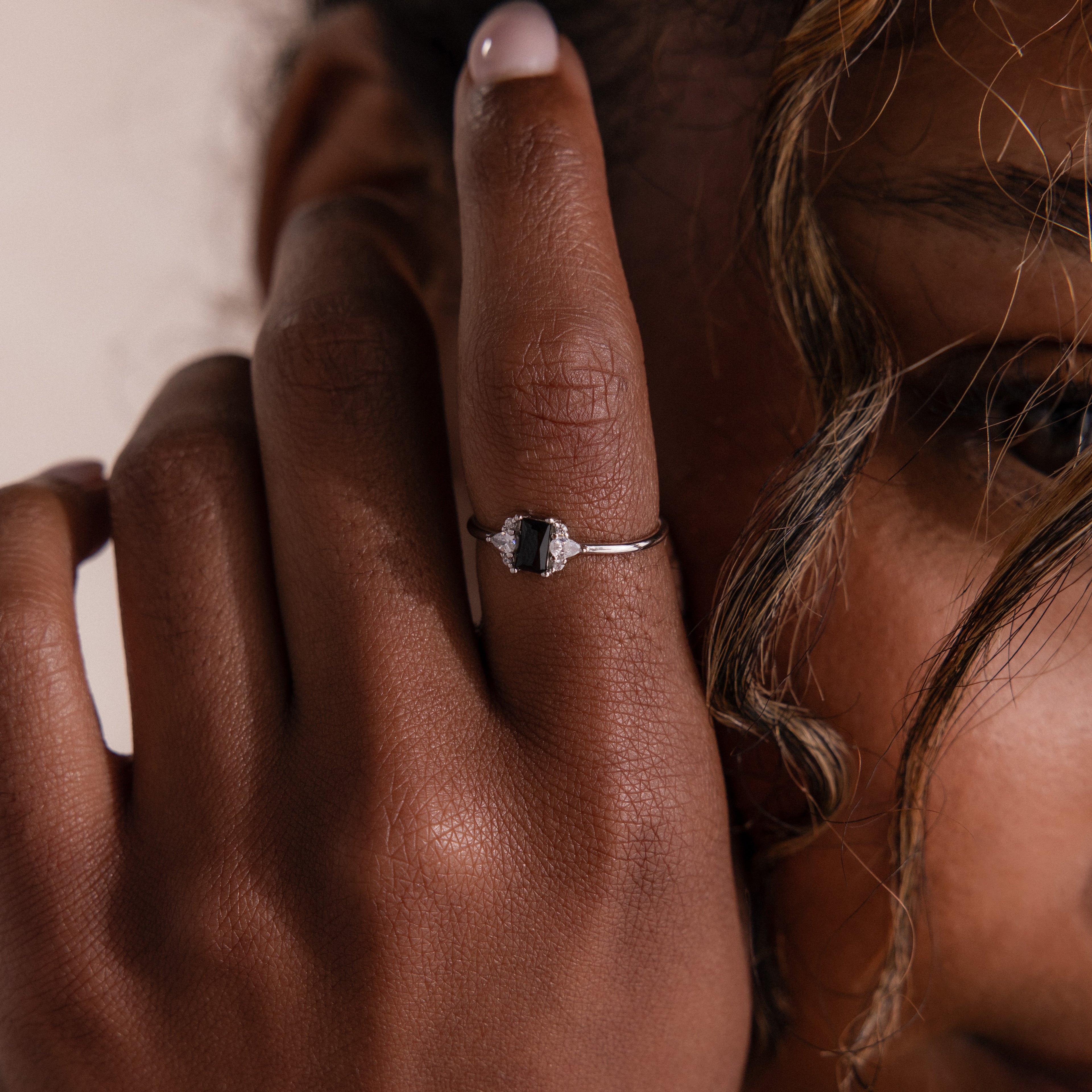 Close-up of a person's hand near their face, showcasing the Black Baguette Diamond Ring in Sterling Silver with a striking baguette-cut black diamond centerpiece.