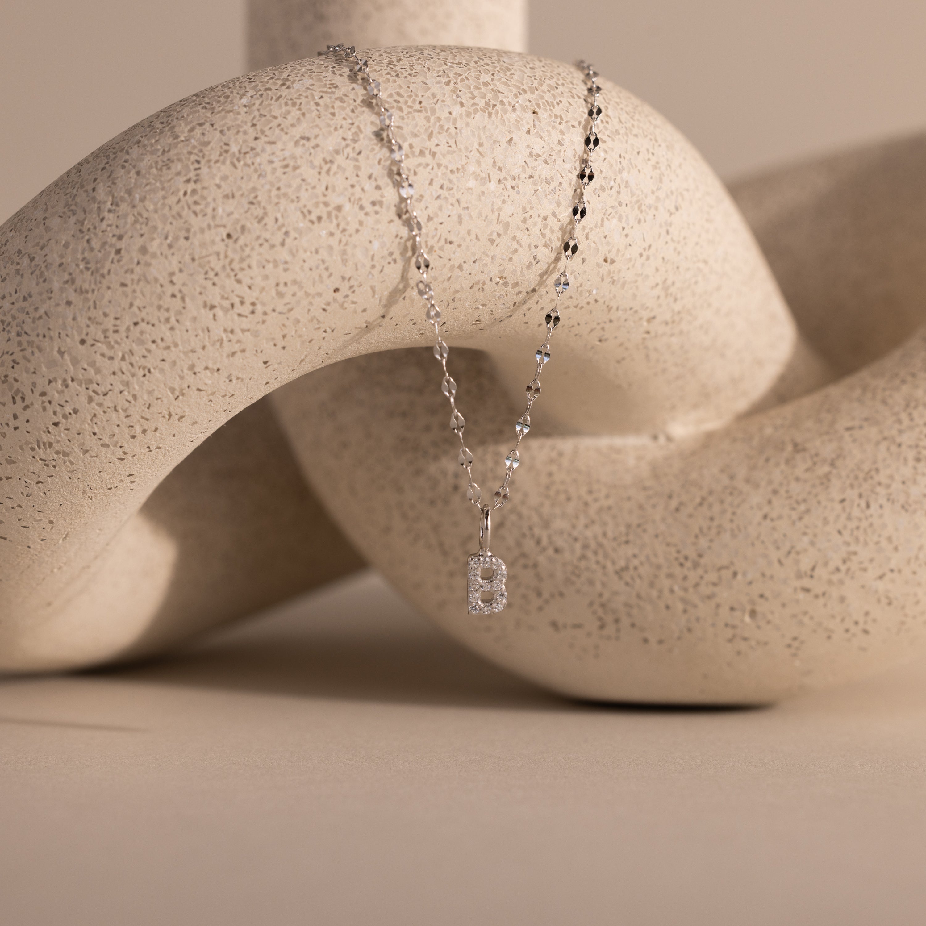 Dainty Pave Letter Necklace in Sterling Silver, featuring a rectangular pendant on a silver chain and displayed on an abstract beige sculpture—a perfect necklace for subtle elegance.