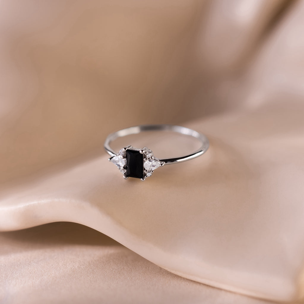 Black Baguette Diamond Ring in Sterling Silver featuring a baguette-cut centerpiece and sparkling clear gems, elegantly displayed on soft beige fabric for a vintage-inspired style.