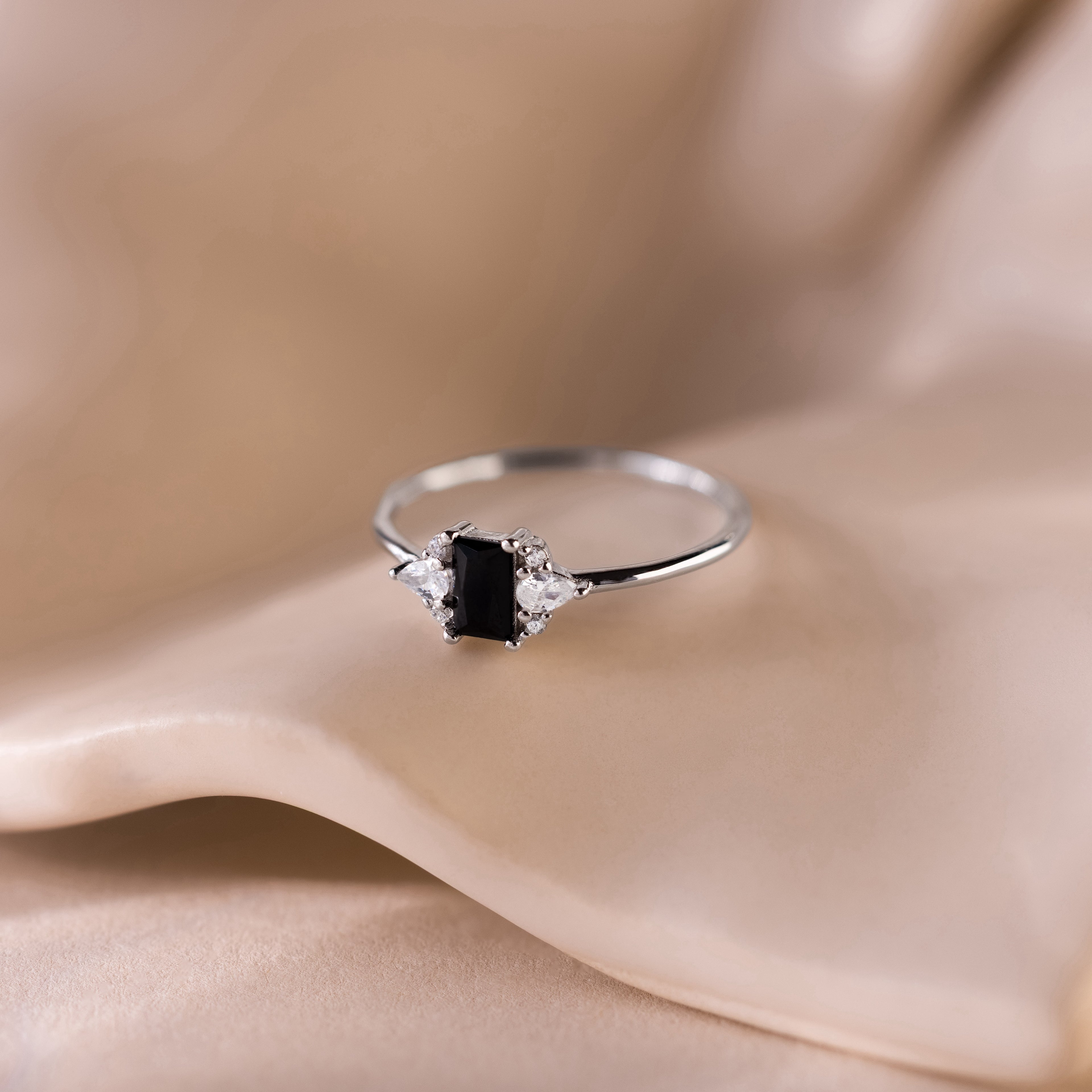 Black Baguette Diamond Ring in Sterling Silver featuring a baguette-cut centerpiece and sparkling clear gems, elegantly displayed on soft beige fabric for a vintage-inspired style.