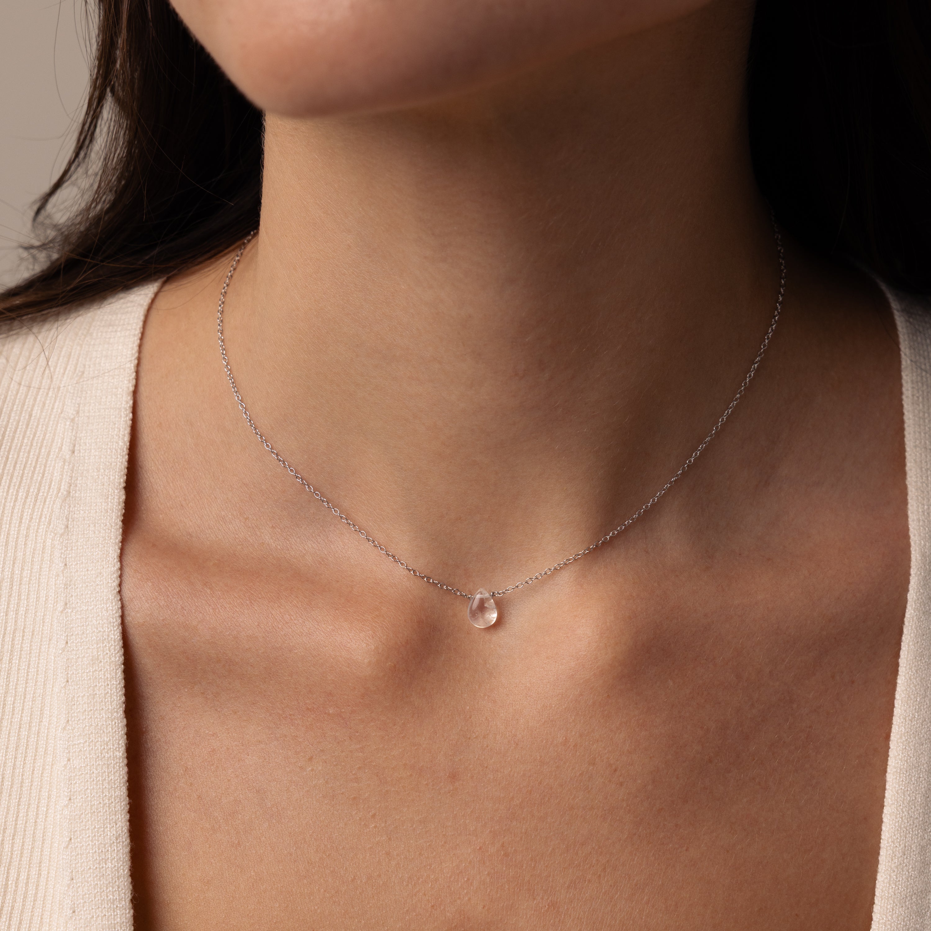 A woman wears the Teardrop Moonstone Necklace in Sterling Silver—a minimalist, elegant chain featuring a small, clear teardrop moonstone pendant.
