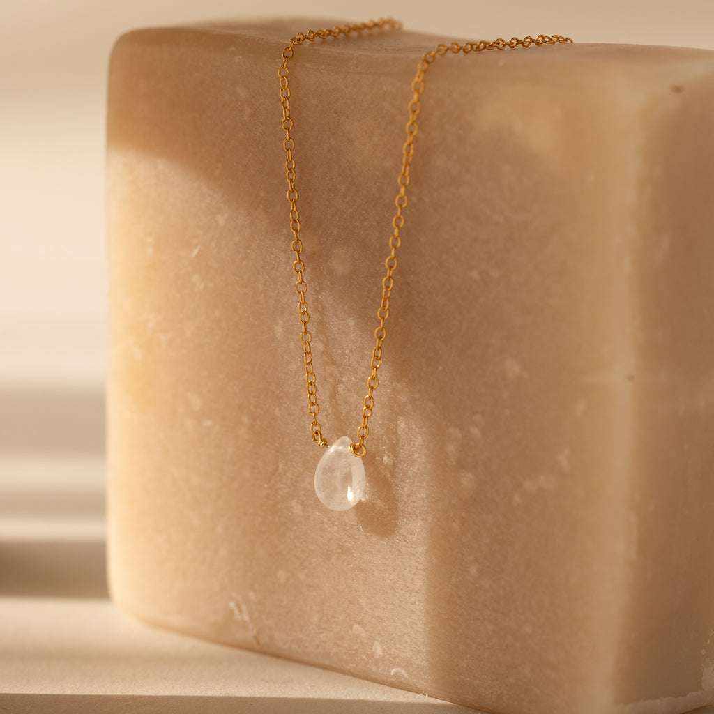 The Teardrop Moonstone Necklace in 18K Gold rests gracefully on a large beige soap bar, bringing minimalist elegance to your jewelry collection.