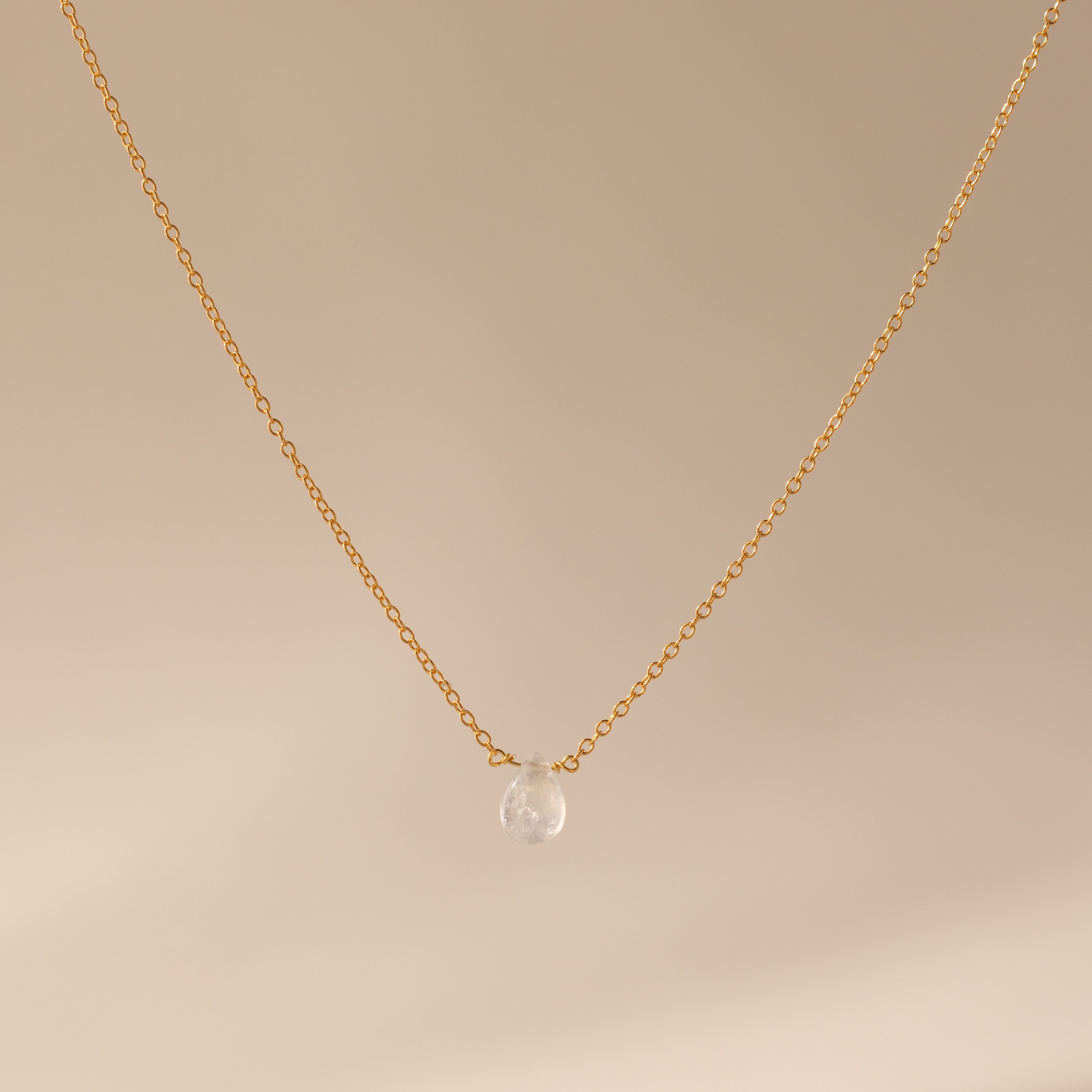 Minimalist jewelry: Teardrop Moonstone Necklace with a gold chain and a single moonstone pendant, shown against a neutral beige background.