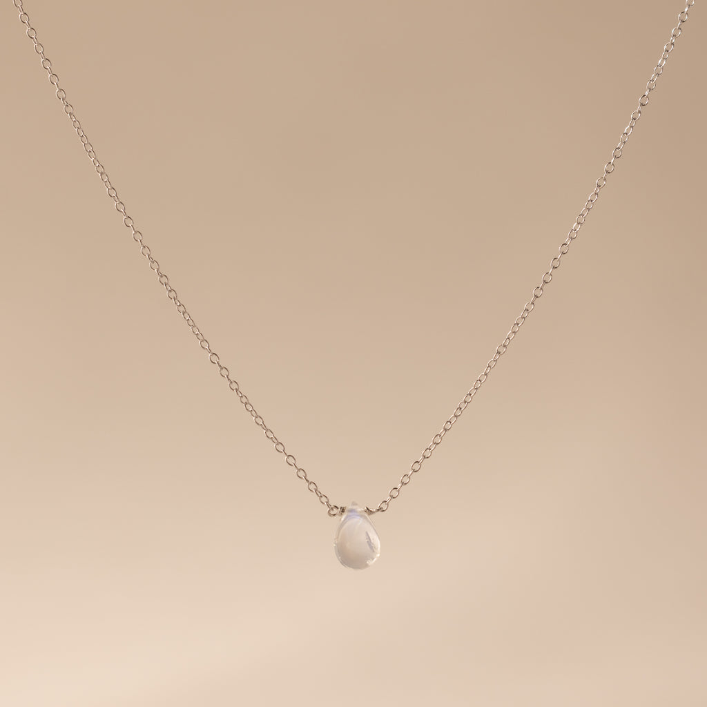 A delicate sterling silver necklace featuring a teardrop moonstone pendant, perfect for lovers of minimalist jewelry, displayed on a beige background.