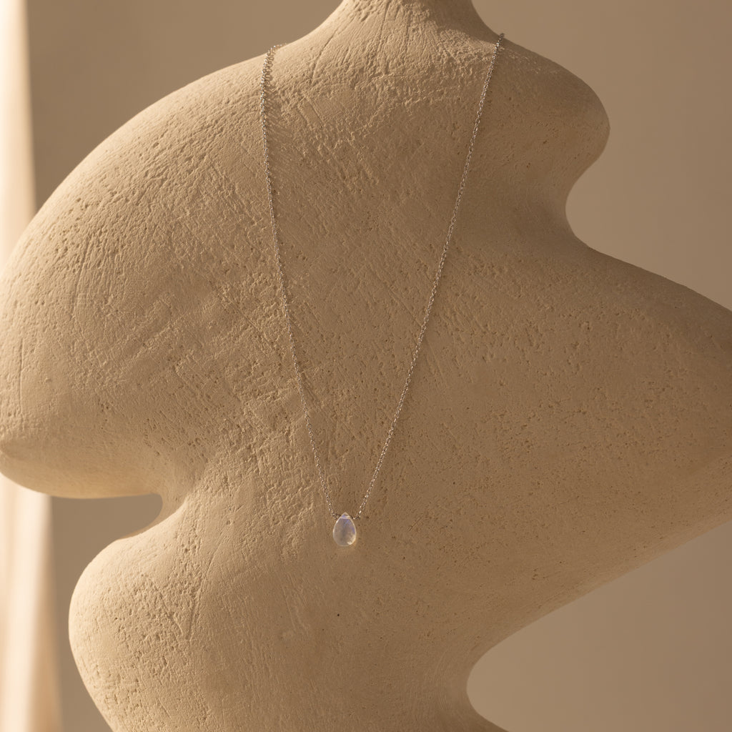 The Teardrop Moonstone Necklace in Sterling Silver is displayed on a textured beige sculpture—an elegant, minimalist piece perfect for moonstone jewelry lovers.