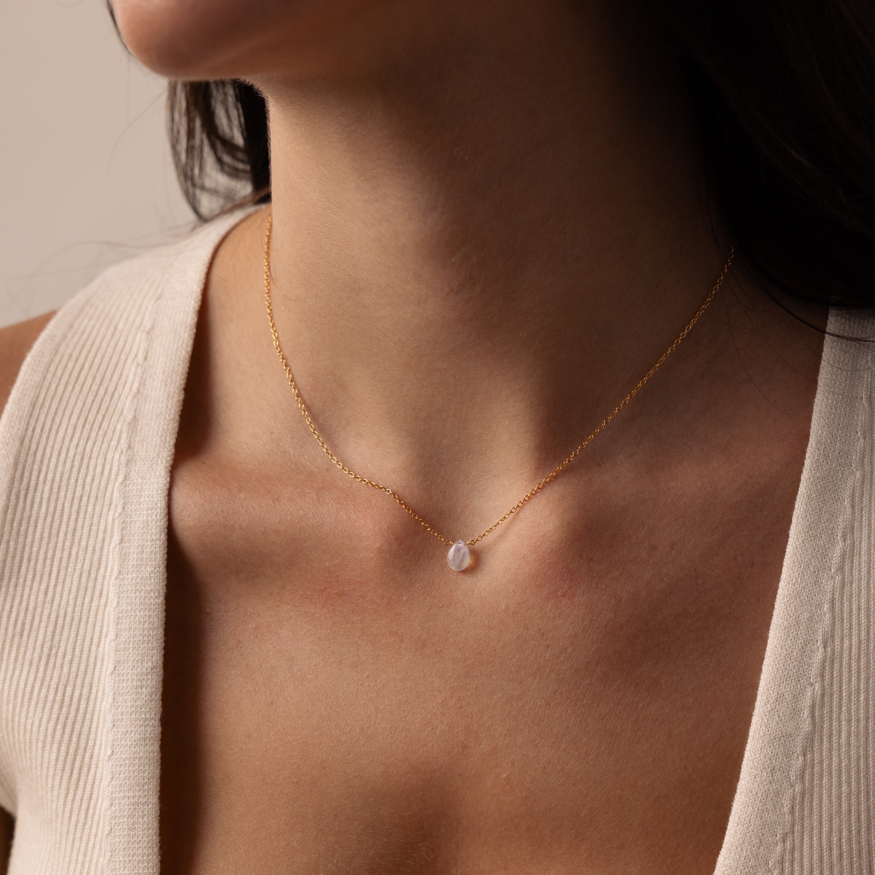 A woman wears the Teardrop Moonstone Necklace, a minimalist gold piece with a small oval pendant, styled with a cream ribbed top.
