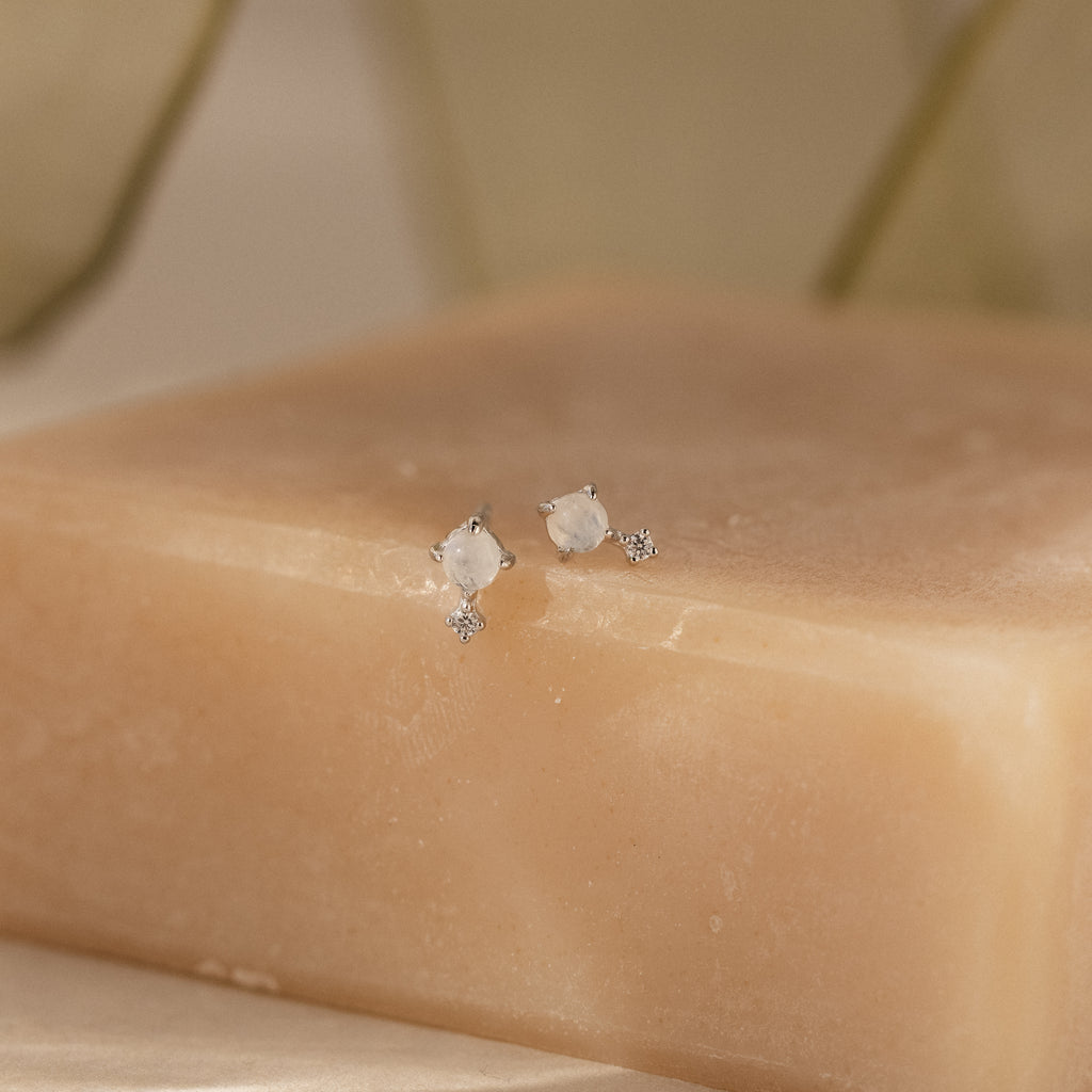 A pair of Moonstone Orbit Studs in Sterling Silver are displayed on a beige soap bar against a soft, neutral background.