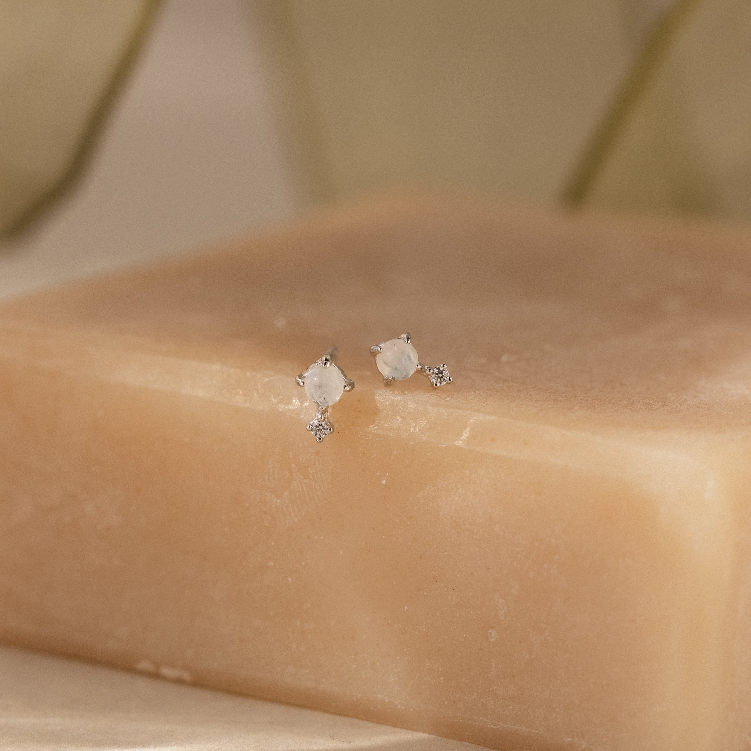 A pair of Moonstone Orbit Studs in Sterling Silver are displayed on a beige soap bar against a soft, neutral background.