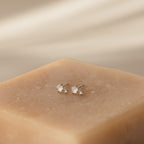 A pair of Moonstone Orbit Studs in sterling silver with small white stones displayed on a beige textured block.