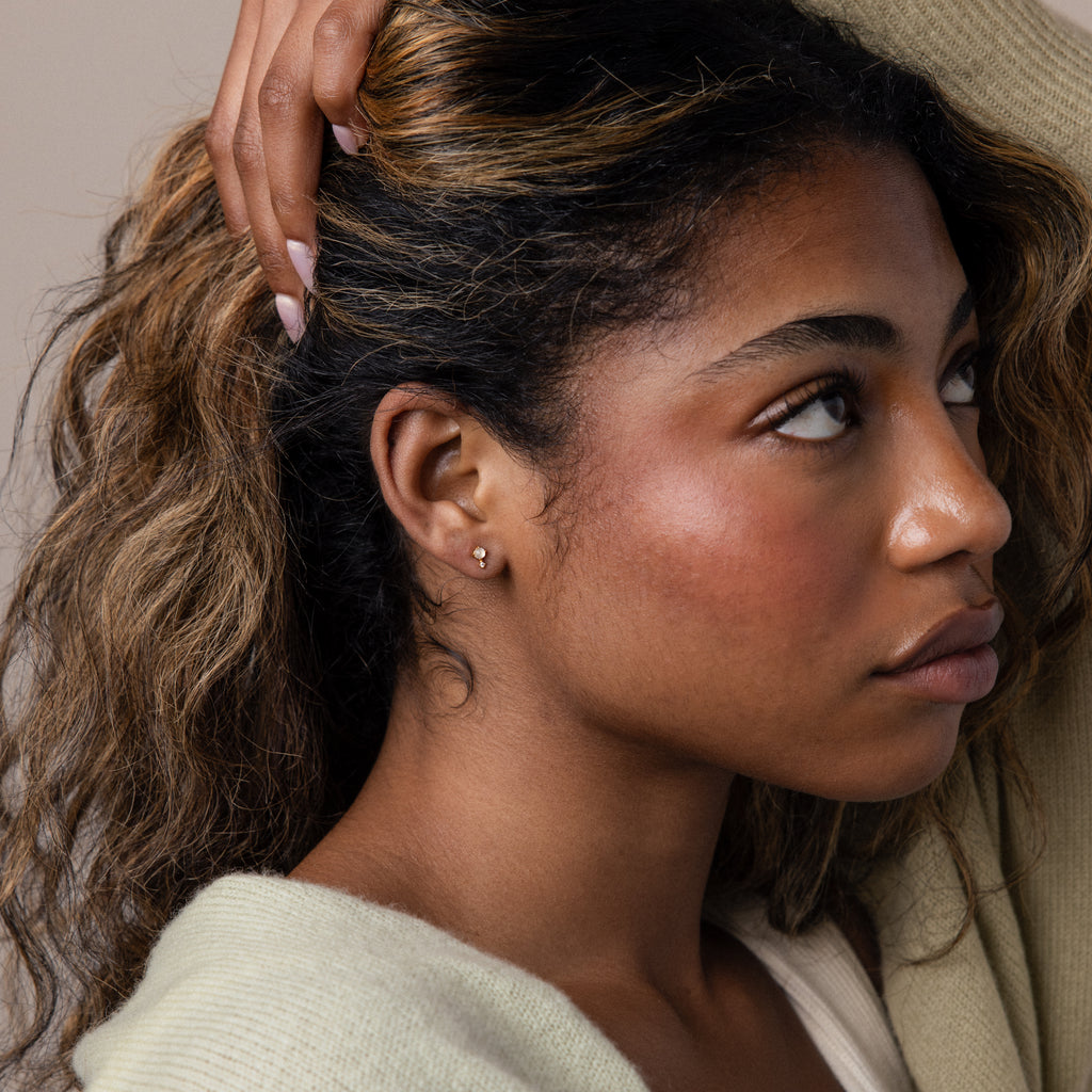 Woman with wavy hair looking to the side, wearing a cream sweater and elegant Moonstone Orbit Studs.