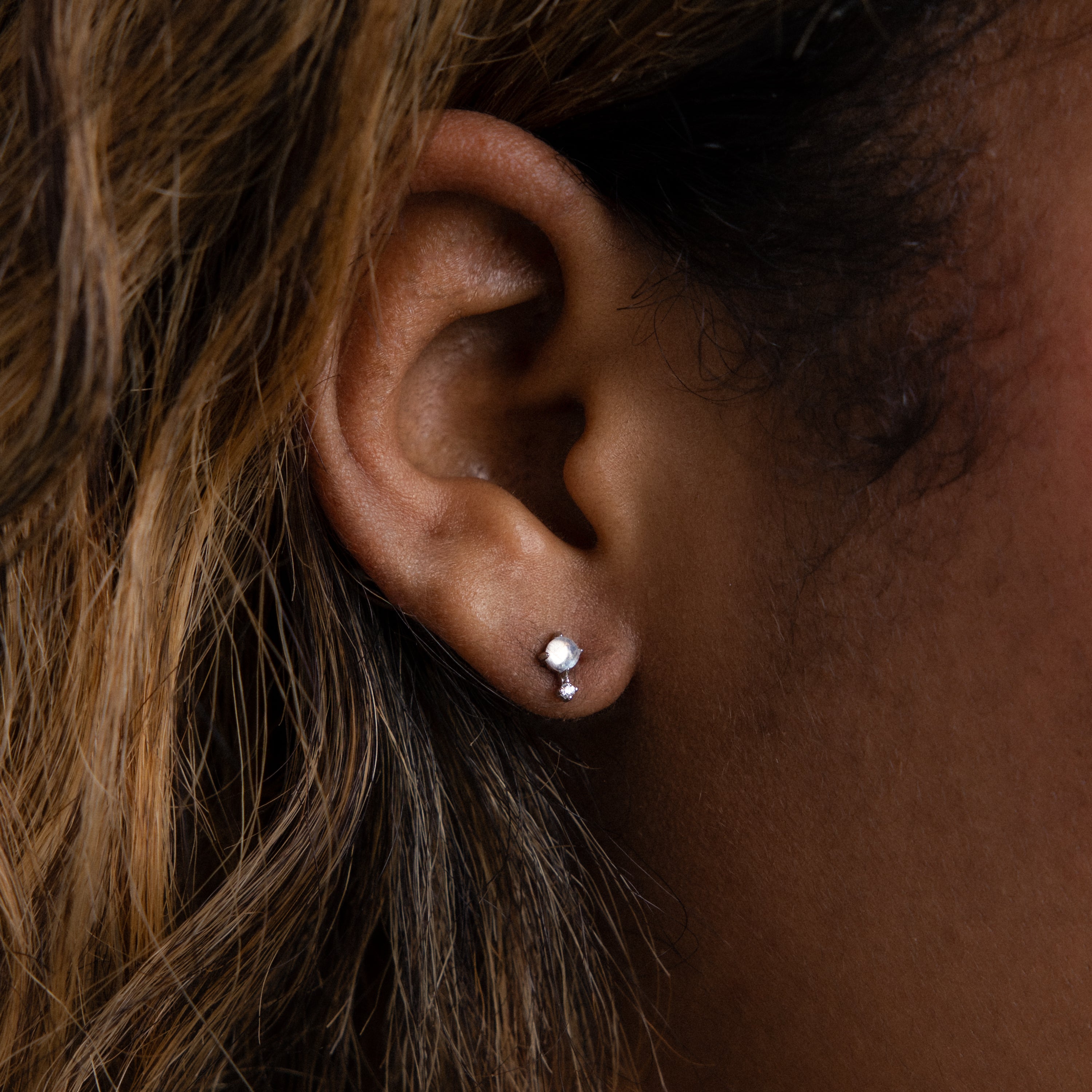 Close-up of a person's ear adorned with Moonstone Orbit Studs in Sterling Silver, partially framed by brown hair.