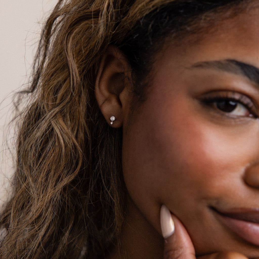 Close-up of a woman smiling, wearing Moonstone Orbit Studs with delicate diamond accents, her hand resting on her chin.