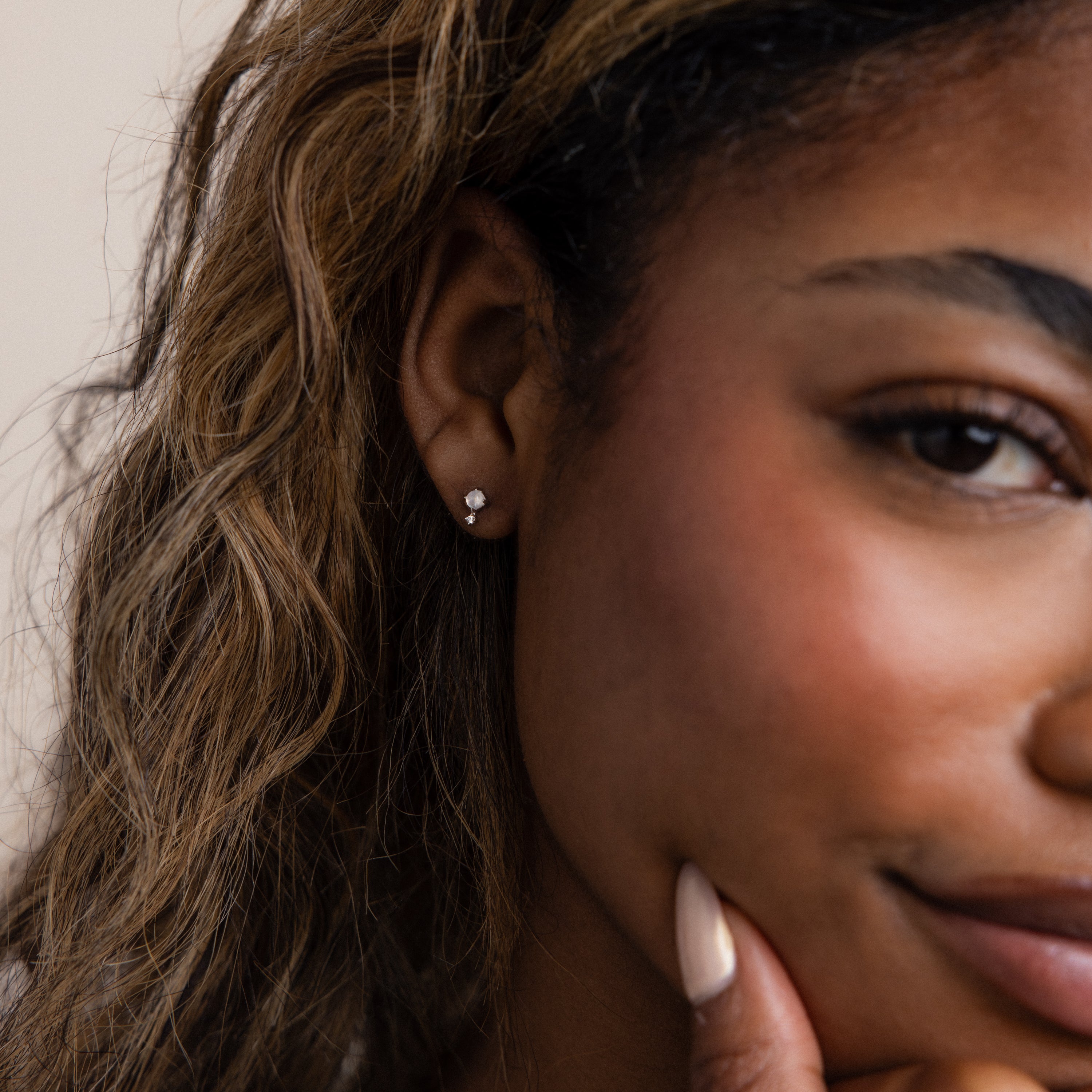 Close-up of a woman smiling, wearing Moonstone Orbit Studs with delicate diamond accents, her hand resting on her chin.