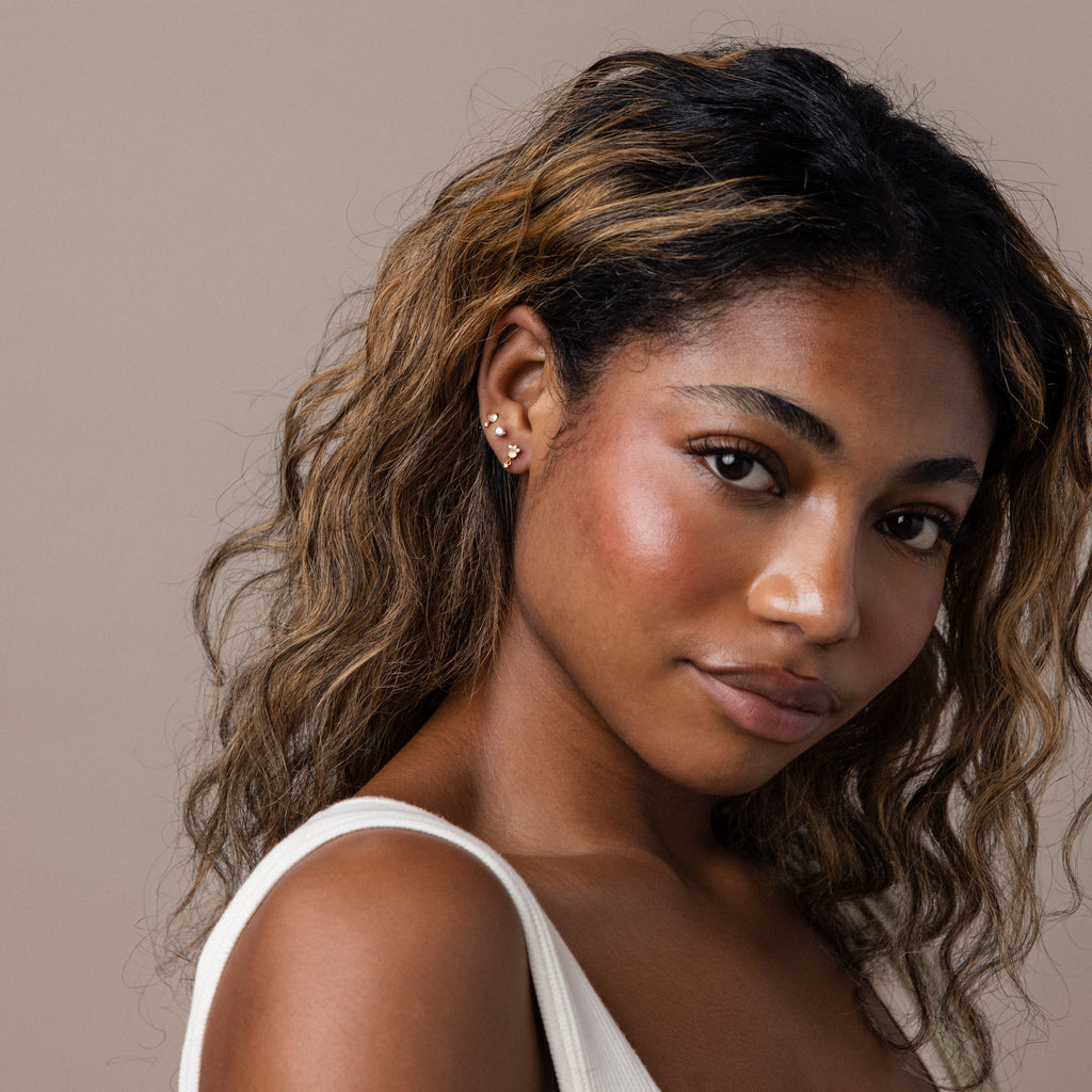Woman with wavy, highlighted hair, wearing Moonstone Orbit Studs and a white top, looking at the camera.