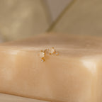 The Moonstone Orbit Studs in 18K Gold are displayed on a beige soap bar with a soft, neutral background.