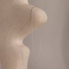 The Dot Station Necklace in Sterling Silver, featuring a delicate chain, is draped over a textured abstract beige sculpture set against a soft, neutral background.