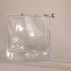 A delicate Dot Station Necklace in Sterling Silver is draped over a clear, wavy glass block with a silver rod on top, highlighting the minimalist piece’s refined elegance.