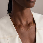 A close-up of a person wearing the Dot Station Necklace in 18K Gold paired with a cream-colored blazer.