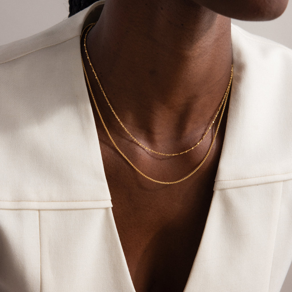 A person in a cream blazer wearing two delicate gold chain necklaces, including a minimalist necklace and the Dot Station Necklace in Sterling Silver.