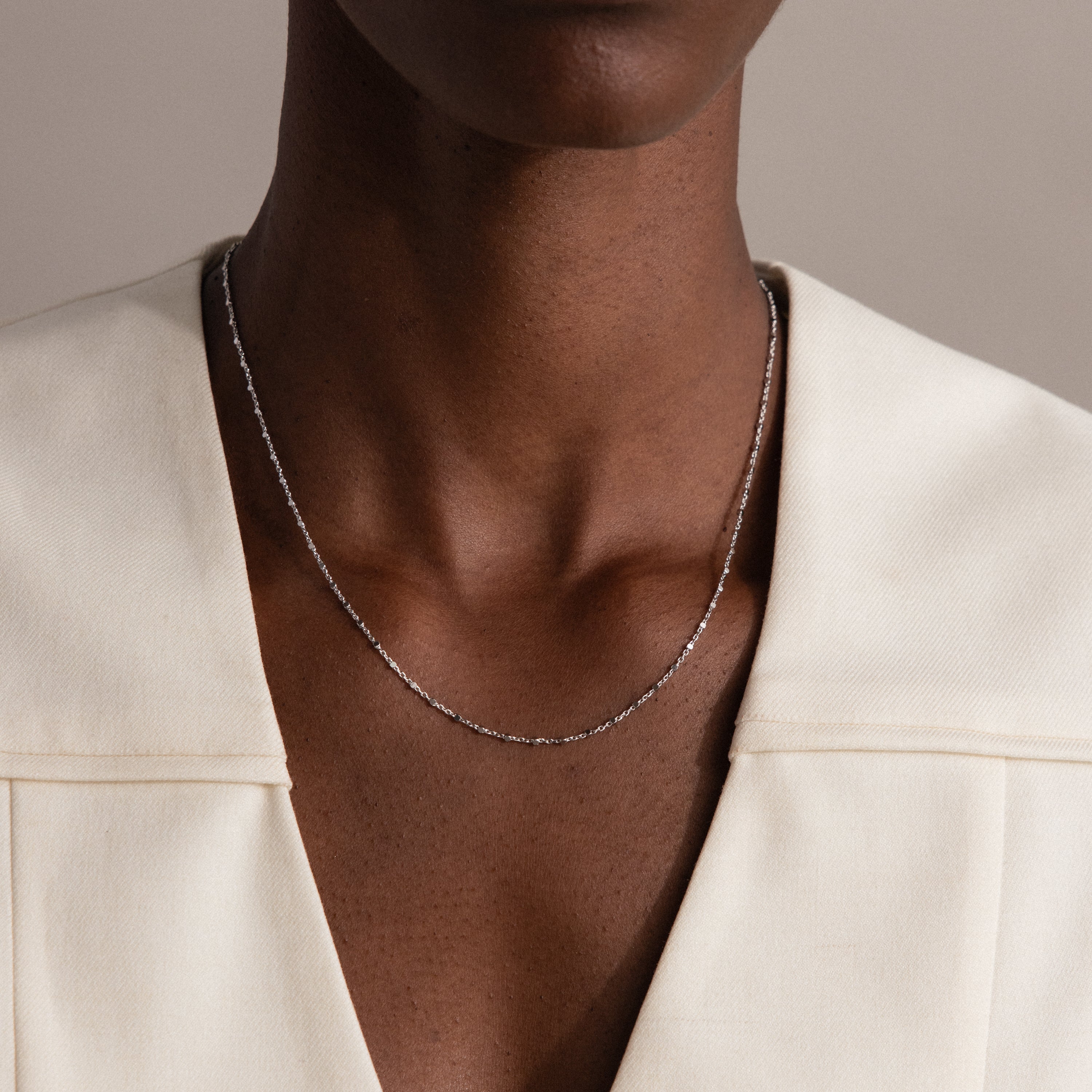 A person wears the Dot Station Necklace, a delicate chain, paired with a cream-colored top, shown from neck to chest.