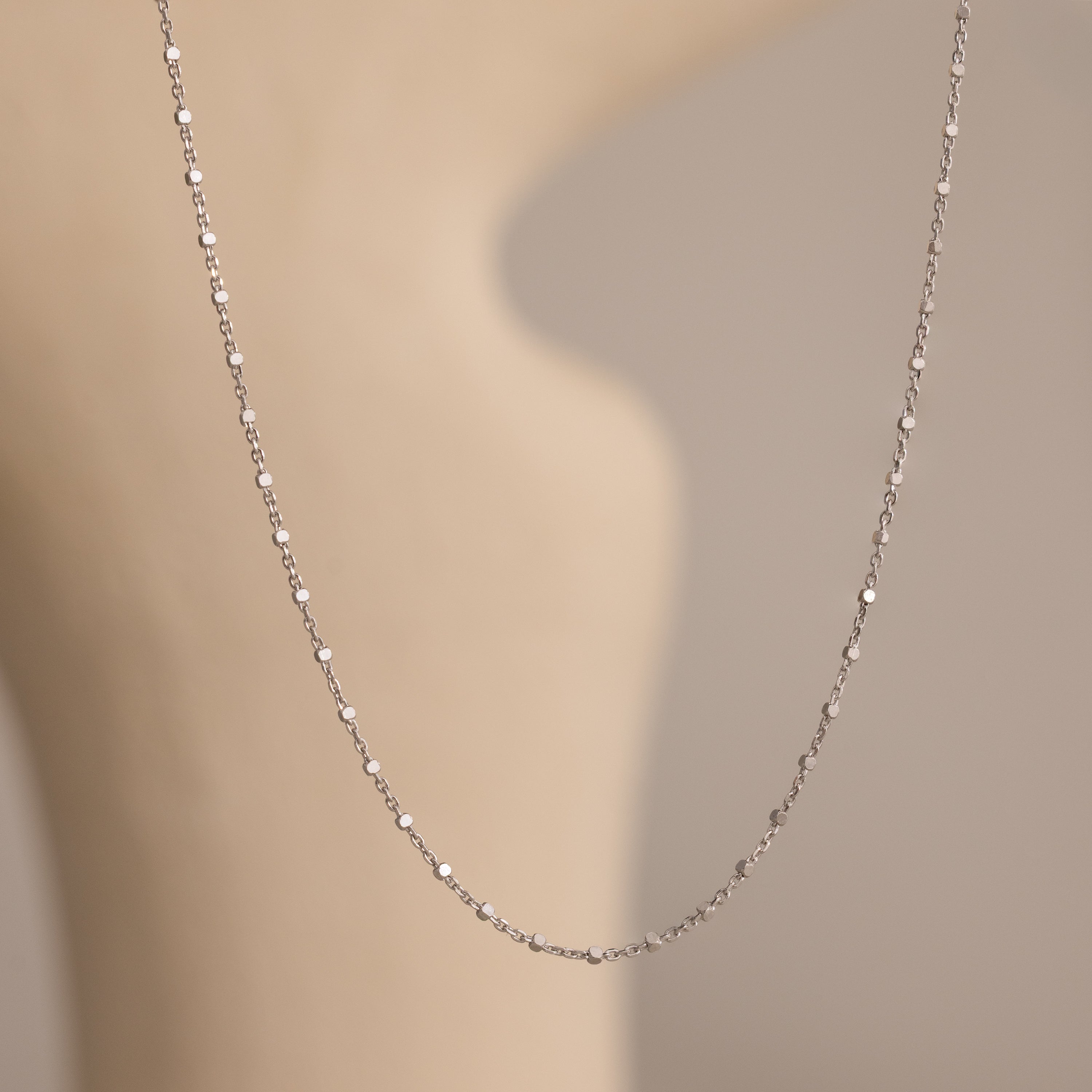The Dot Station Necklace in Sterling Silver is displayed on a blurred, beige background.