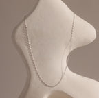 The Dainty Paperclip Necklace in Sterling Silver drapes elegantly over an abstract white sculptural form, highlighting the modern sophistication of this delicate piece.