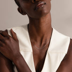 A woman wears a sleeveless white top and the Dainty Paperclip Necklace in Sterling Silver, posing with one hand on her shoulder—an ideal piece for layering with other modern jewelry.