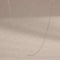 The Dainty Paperclip Necklace in Sterling Silver features small oval links and is shown against a neutral beige background—a perfect layering piece for modern jewelry lovers.