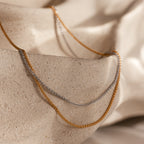 The Woven Chain Necklace draped over textured beige stone, bathed in soft, natural lighting.