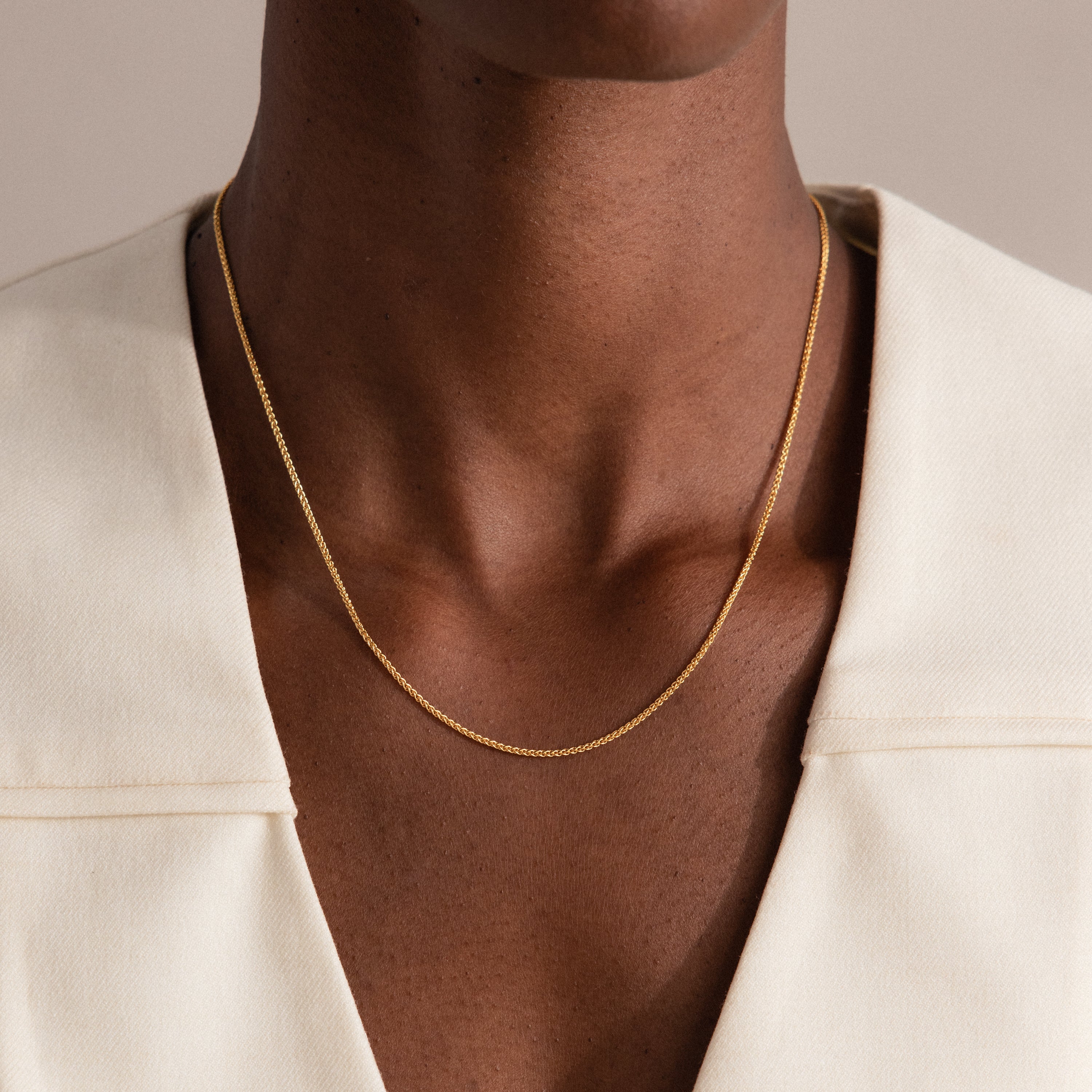 Someone wears the Woven Chain Necklace, a thin gold piece, layered over an off-white V-neck top.