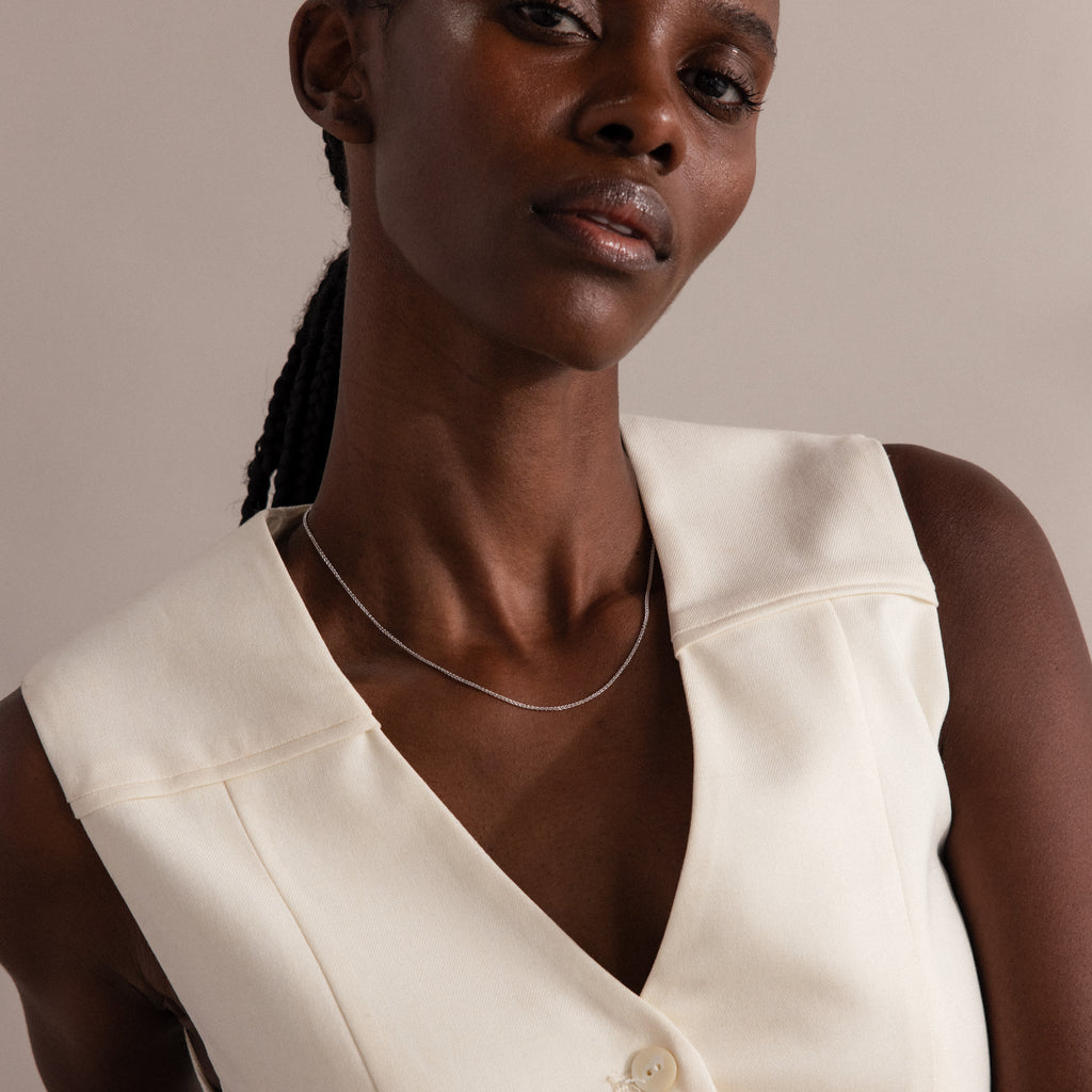 Woman wearing a sleeveless cream vest and the Woven Chain Necklace in Sterling Silver, looking confidently at the camera.
