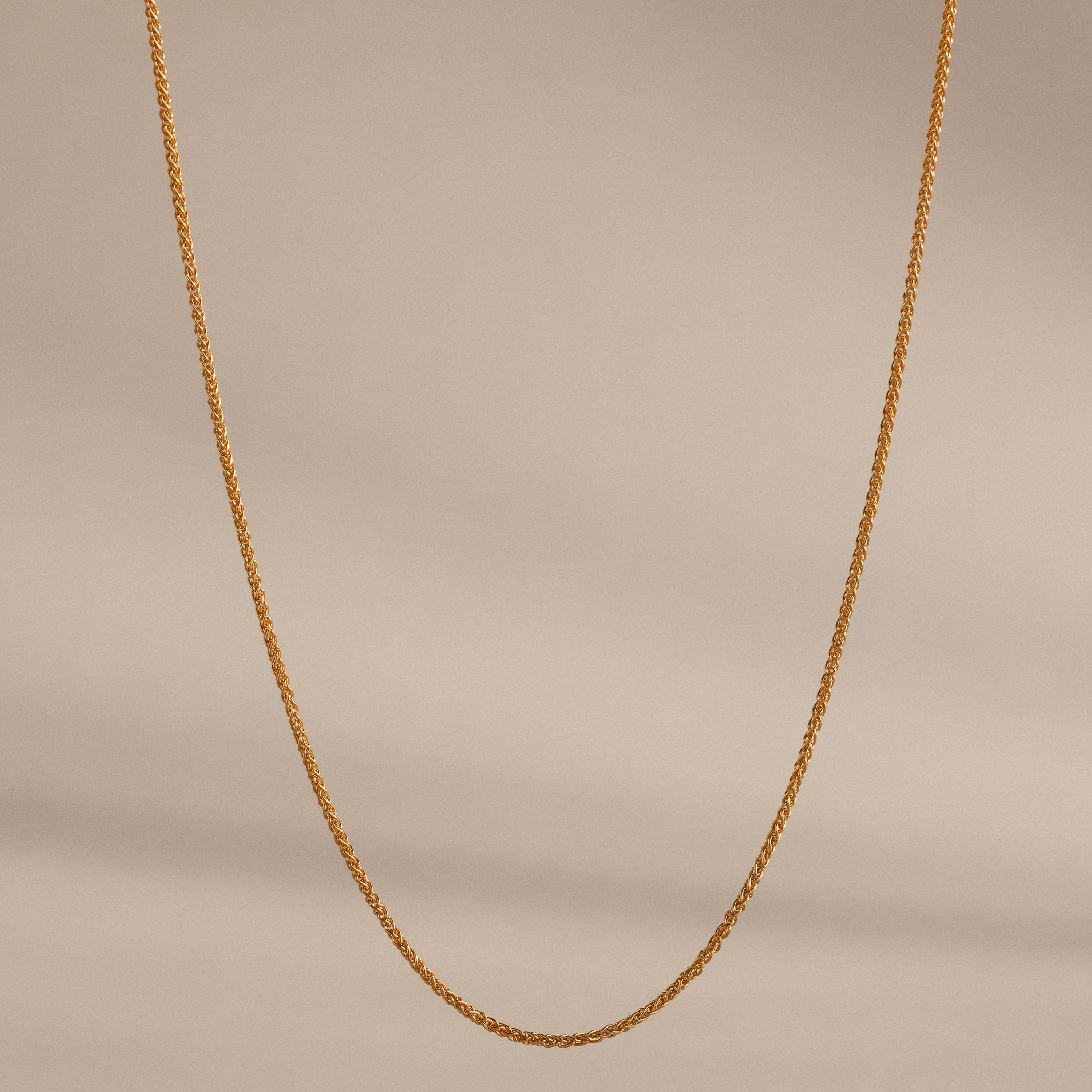 The Woven Chain Necklace in 18K Gold, featuring interlaced links, is displayed against a beige background.
