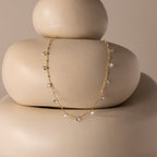 The Satellite Diamond Necklace in 18K Gold, featuring delicate crystal charms, is displayed on smooth, stacked beige stones with a neutral backdrop.