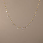 The Satellite Diamond Necklace in 18K Gold features small, evenly spaced clear crystal beads, displayed on a plain beige background.