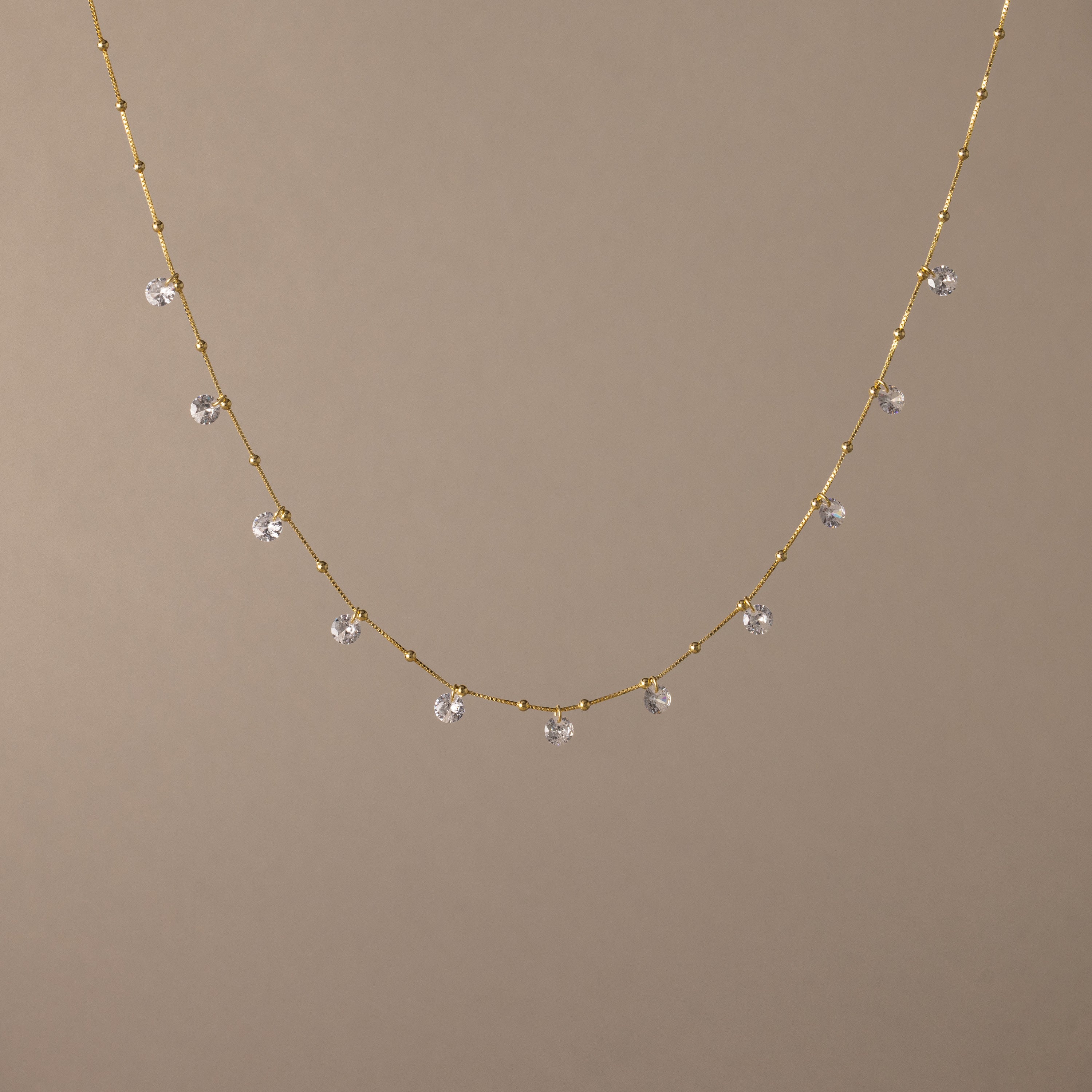The Satellite Diamond Necklace in 18K Gold features small, evenly spaced clear crystal beads, displayed on a plain beige background.
