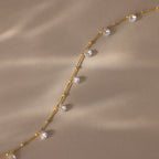 Satellite Diamond Necklace in 18K Gold, featuring spaced round clear gemstones on a beige textured background and softly lit by sunlight. This dainty piece adds delicate sparkle to any look.