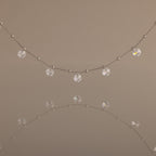 Satellite Diamond Necklace featuring small clear crystal beads, shown reflected on a smooth, neutral surface.