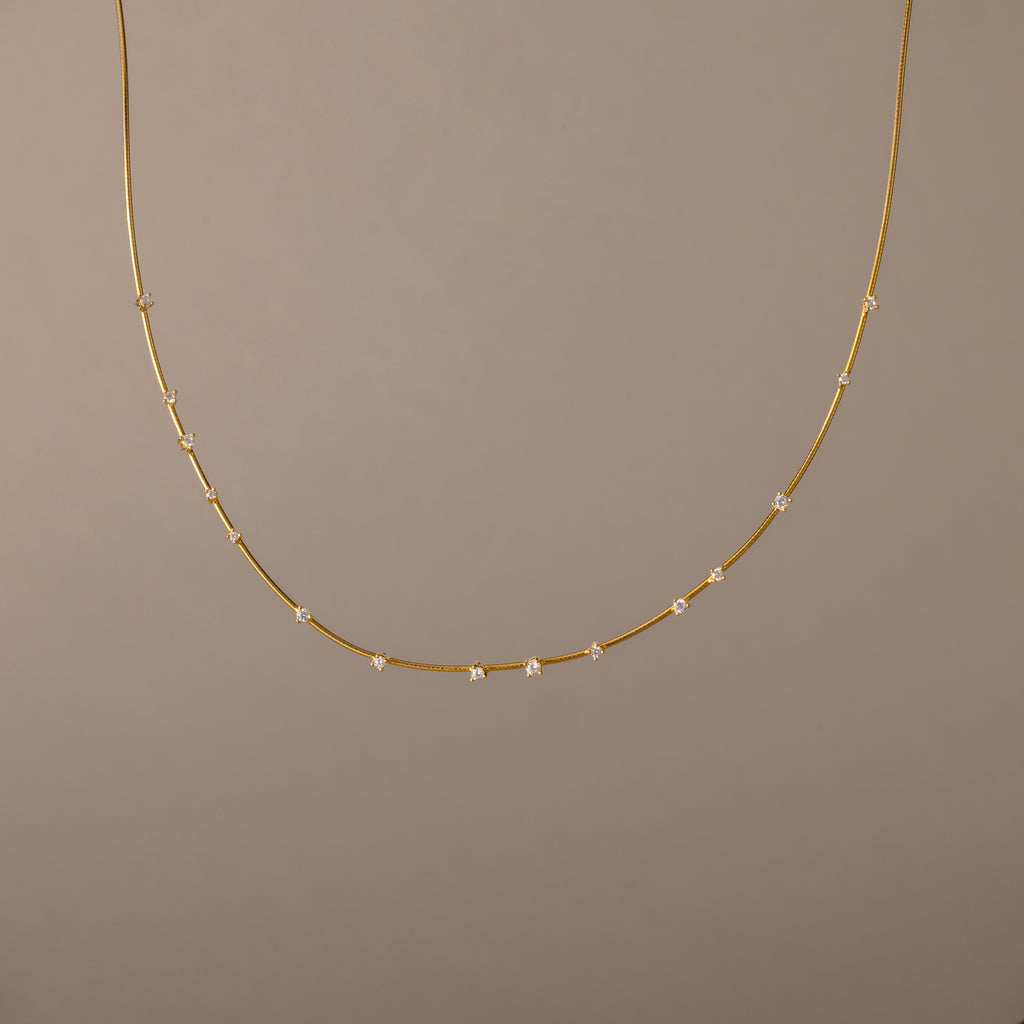 The Sprinkle Diamond Necklace in 18K Gold features a delicate chain adorned with small, evenly spaced diamonds, shown against a plain beige background.