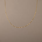The Sprinkle Diamond Necklace in 18K Gold features a delicate chain adorned with small, evenly spaced diamonds, shown against a plain beige background.