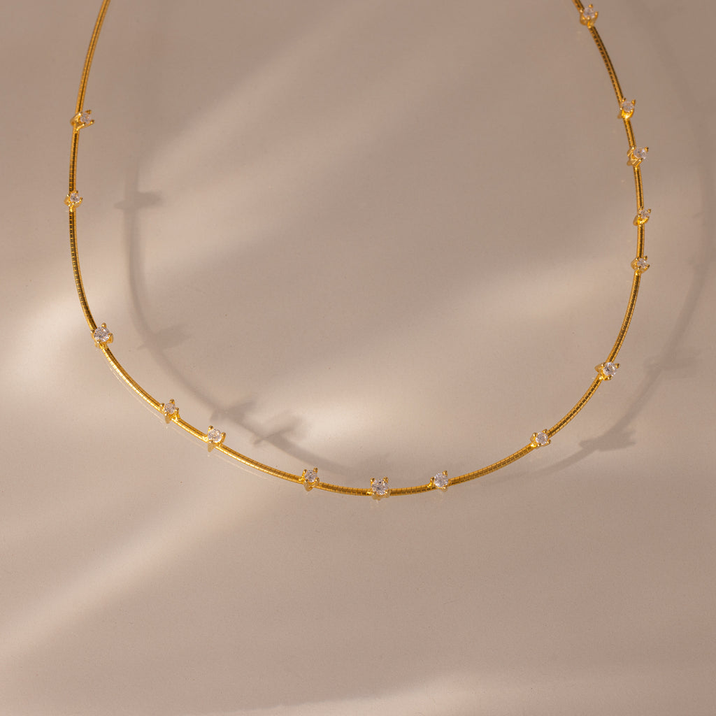 The Sprinkle Diamond Necklace in 18K Gold features delicate gold layering and small, evenly spaced diamonds, showcased on a neutral beige background.