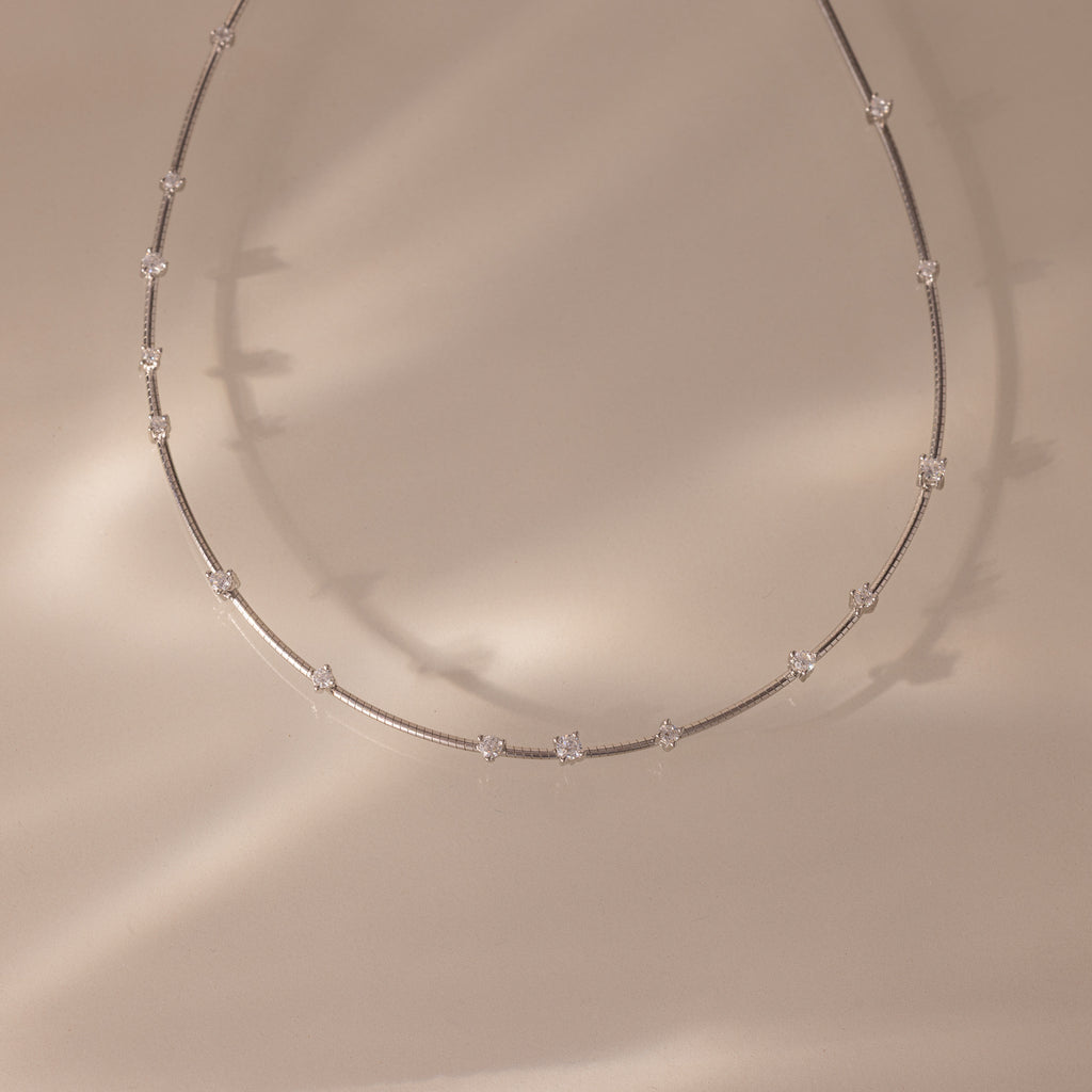 The Sprinkle Diamond Necklace in Silver features a fine, delicate chain with small, evenly spaced diamonds on a soft beige background. Perfect for layering and adding an elegant touch to any look.