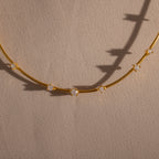 The Sprinkle Diamond Necklace in 18K Gold features a delicate chain adorned with evenly spaced sparkling stones, shown resting on a textured beige surface.